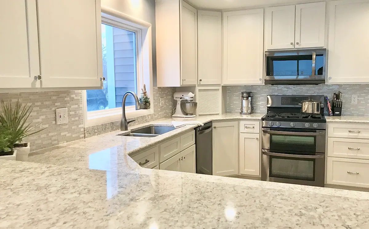 A white kitchen with shaker cabinets, stainless appliances and marble counters